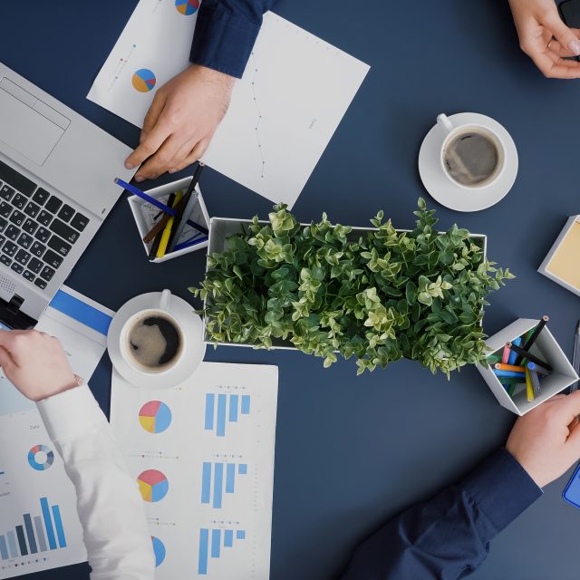 Top view of business group analyzing company infographics documents brainstorming management ideas in startup office. Teamwork discussing financial statistics sharing strategy paperwork