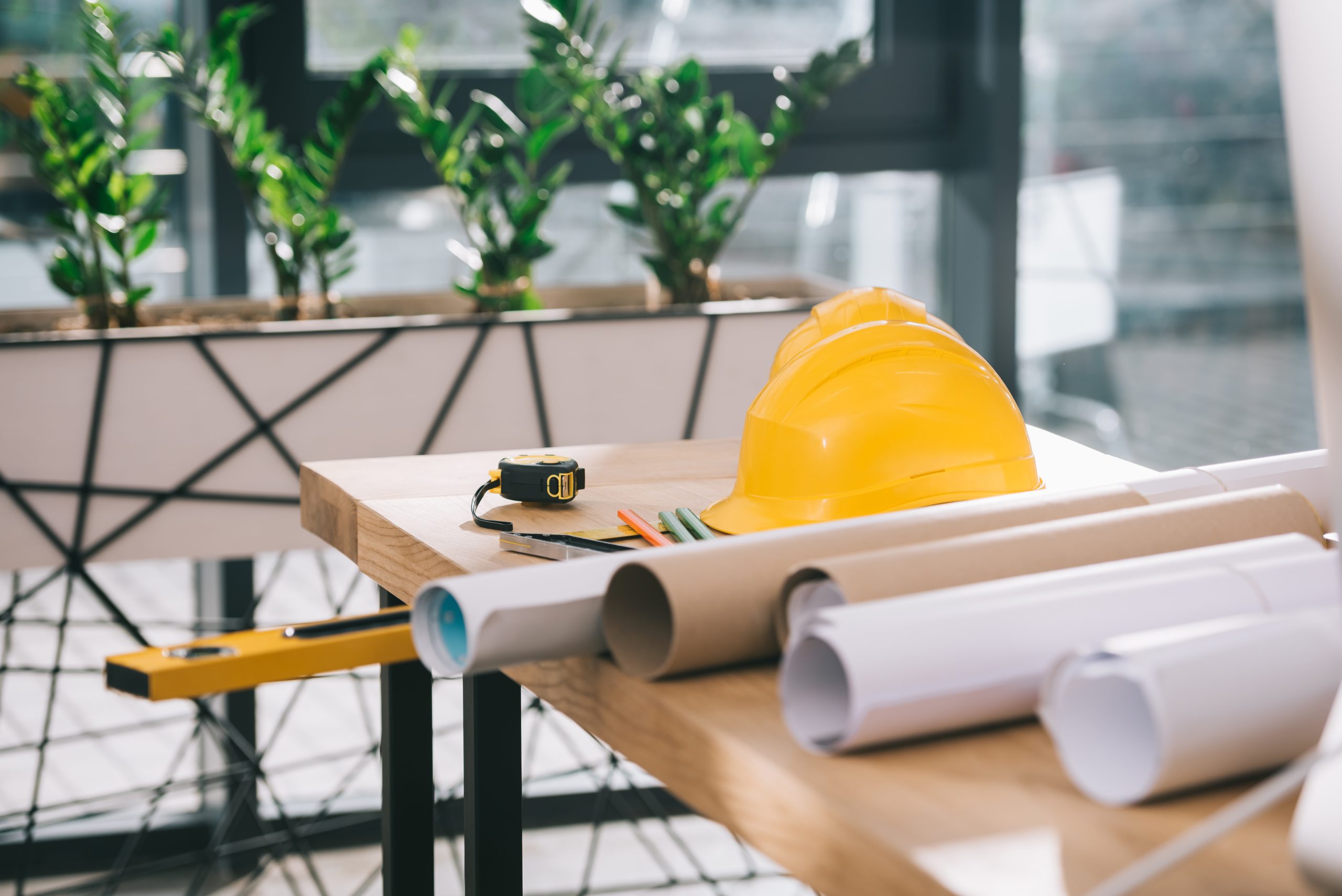 hardhat, tape measure and blueprints on table in modern architect office
