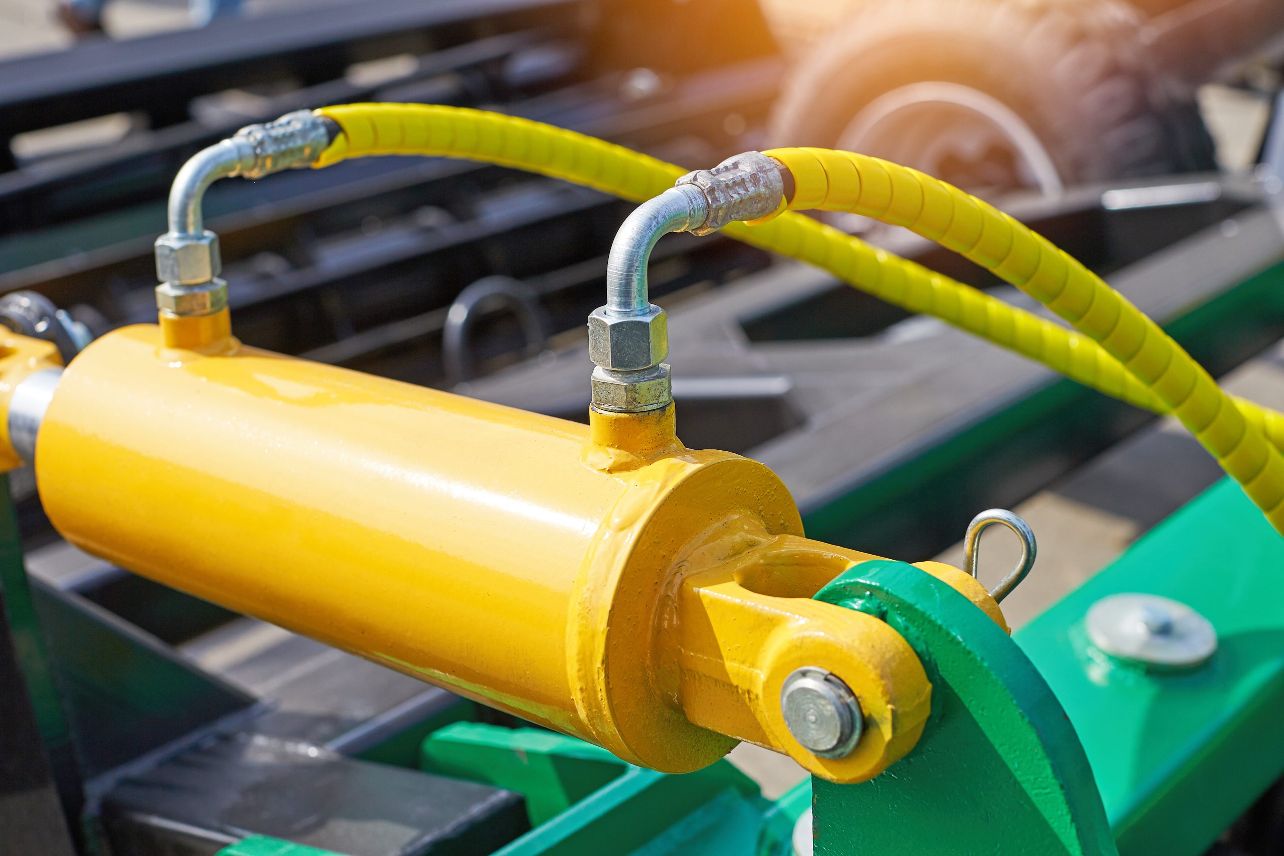 Hydraulic cylinder and yellow hoses on a green frame